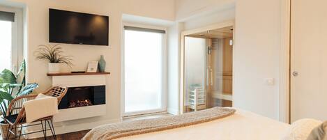 A modern bedroom with a large bed, a fireplace, a TV, and a view of the outside.