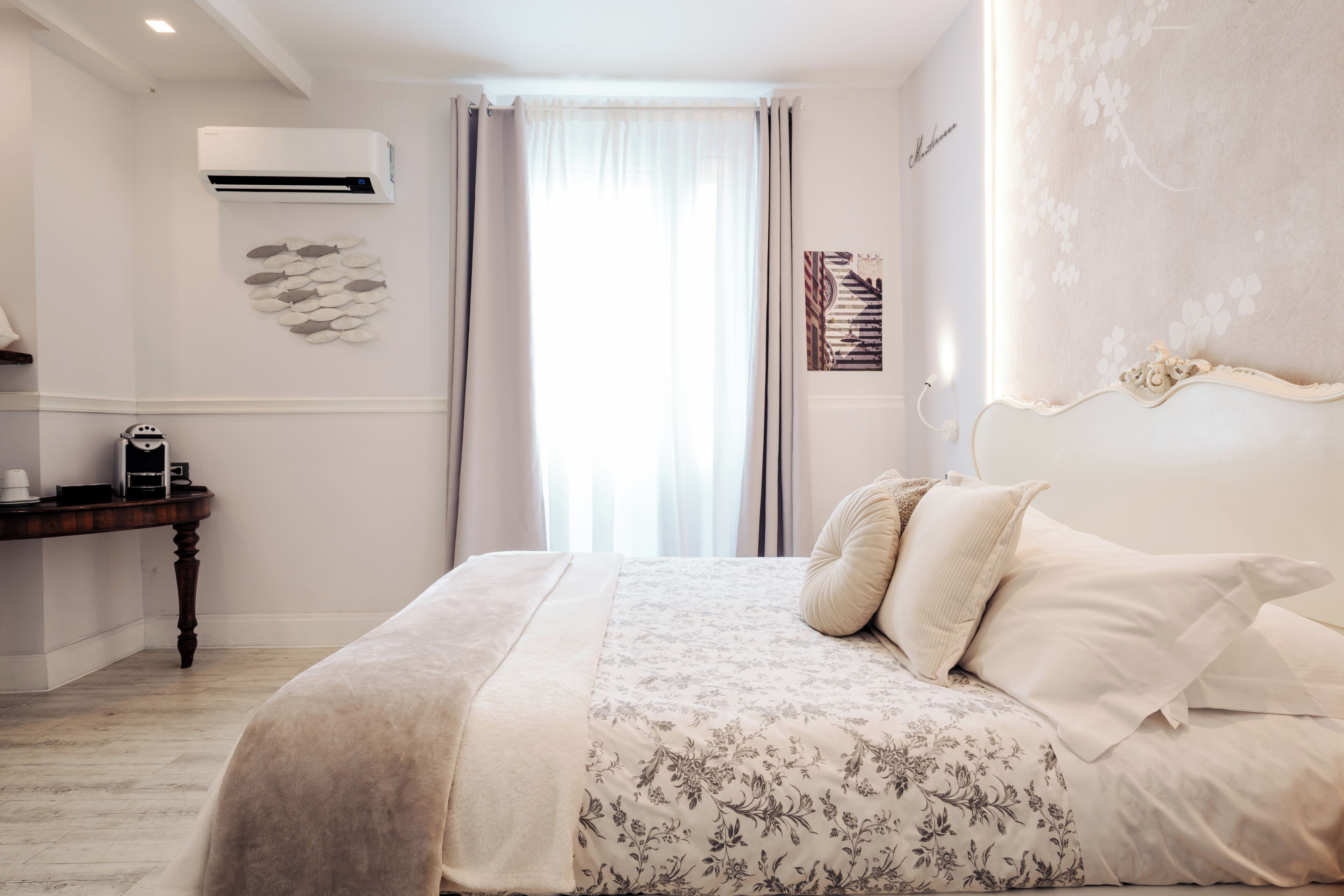 Un dormitorio con cama, mesita de noche, aire acondicionado, ventana con cortinas y un diseño floral en la pared.
