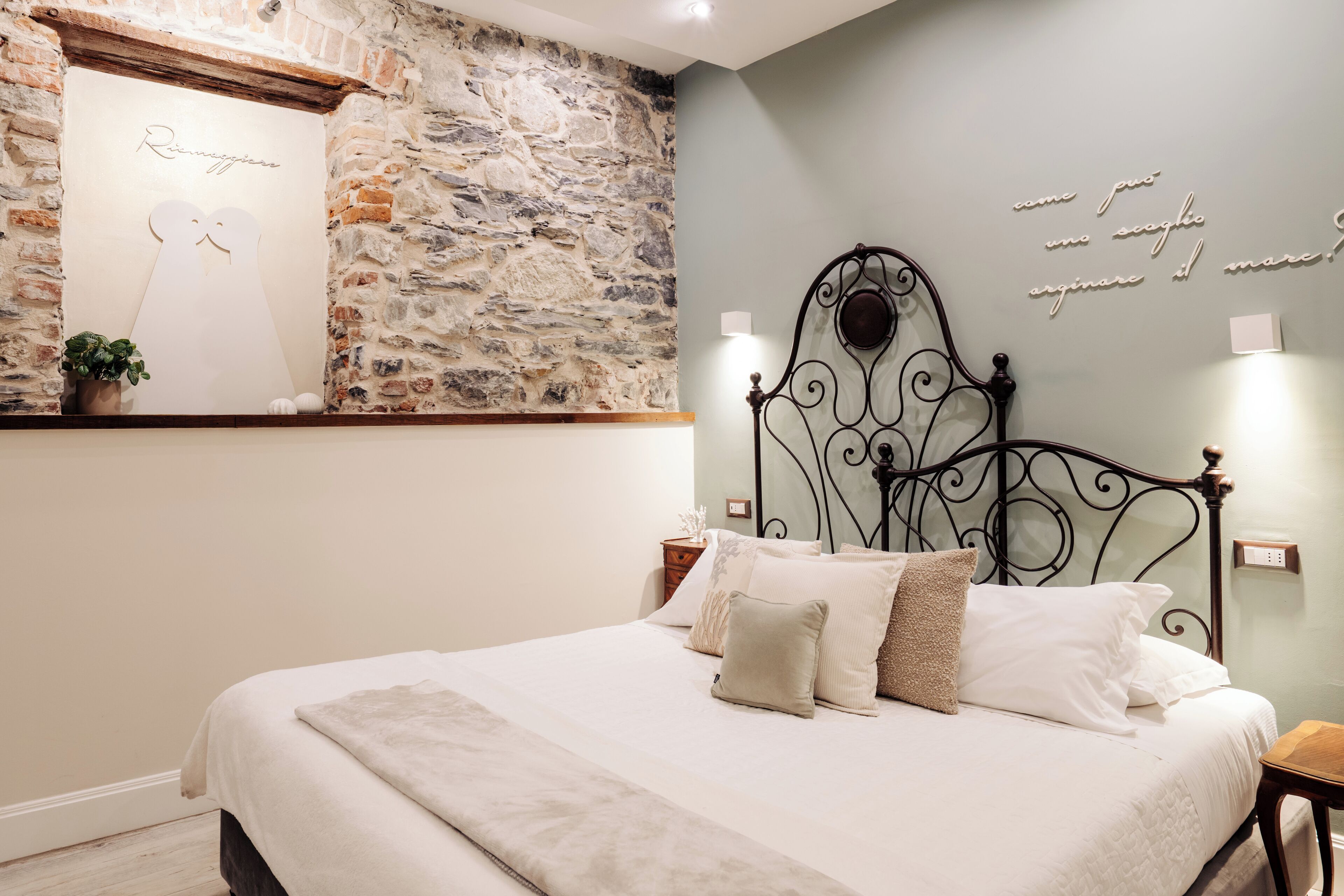 Un dormitorio con pared de piedra, cama con ropa de cama blanca y cabecera decorativa de metal.