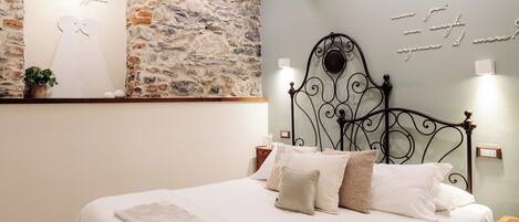 Un dormitorio con pared de piedra, cama con ropa de cama blanca y cabecera decorativa de metal.