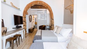 Habitación de hotel con un arco de ladrillo, una cama con ropa blanca, un escritorio con televisor y una pequeña zona de estar.