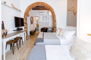 Habitación de hotel con un arco de ladrillo, una cama con ropa blanca, un escritorio con televisor y una pequeña zona de estar.