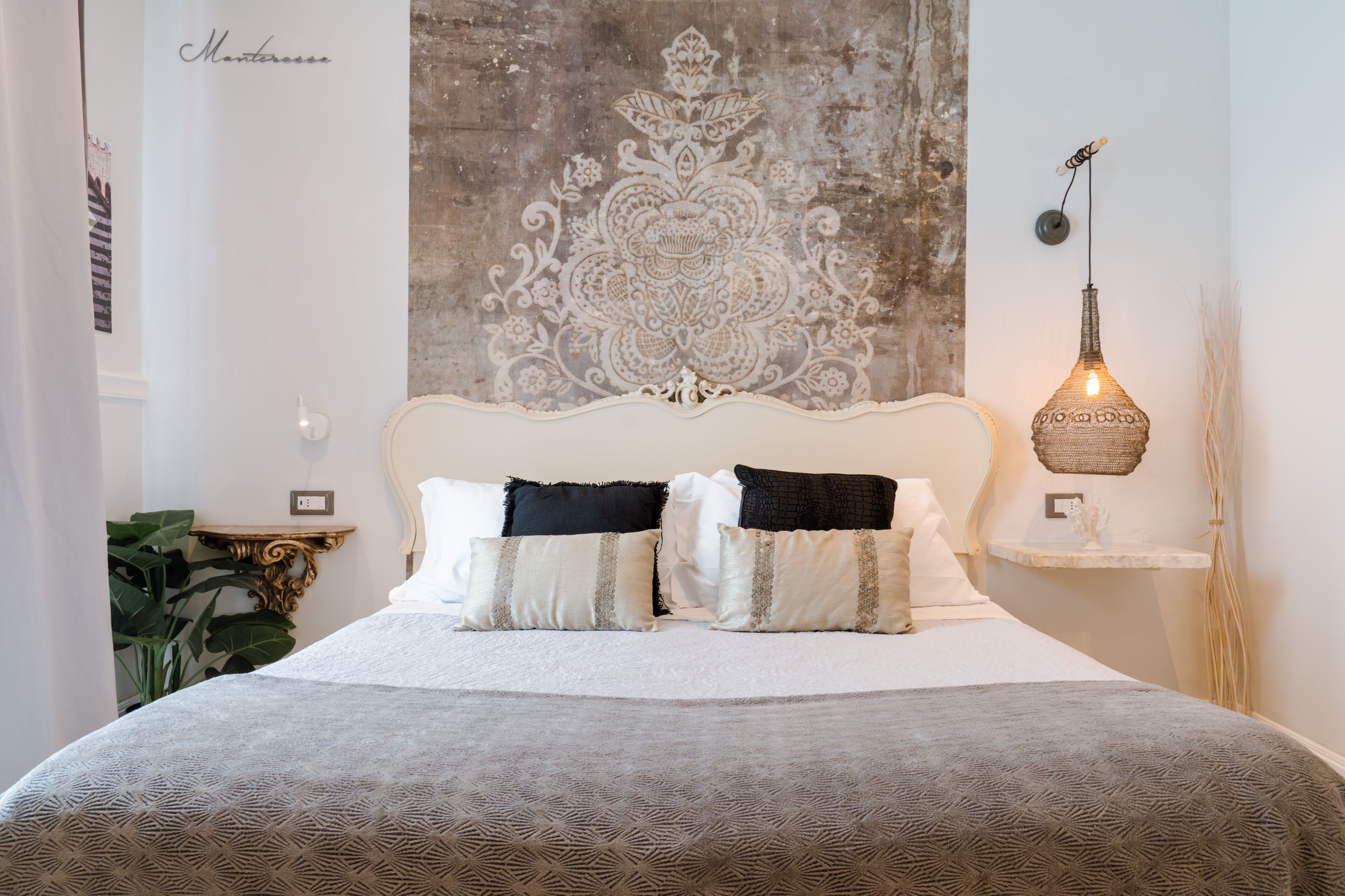 Un lit bien fait, recouvert d’une couvre-lit à motifs, avec une décoration murale au-dessus et un luminaire original fixé au mur.
