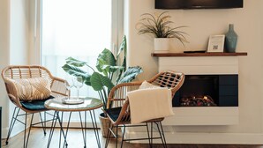 Un salón con chimenea, dos sillones de mimbre, una mesa de vidrio y una planta en maceta.