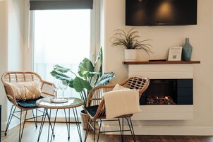 Un salón con chimenea, dos sillones de mimbre, una mesa de vidrio y una planta en maceta.