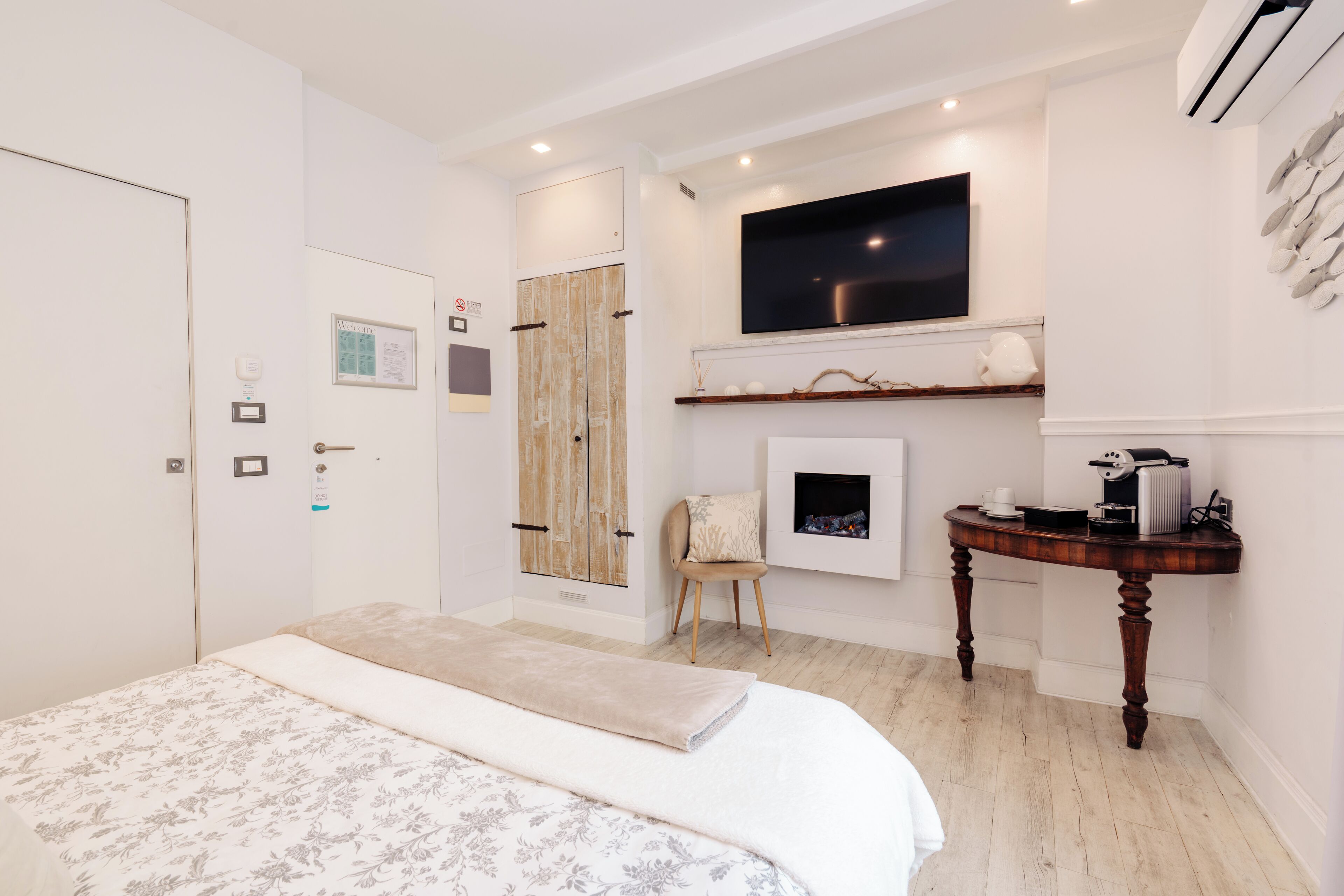 Een slaapkamer met een bed, een televisie boven een open haard, een stoel en een klein tafeltje met een waterkoker.