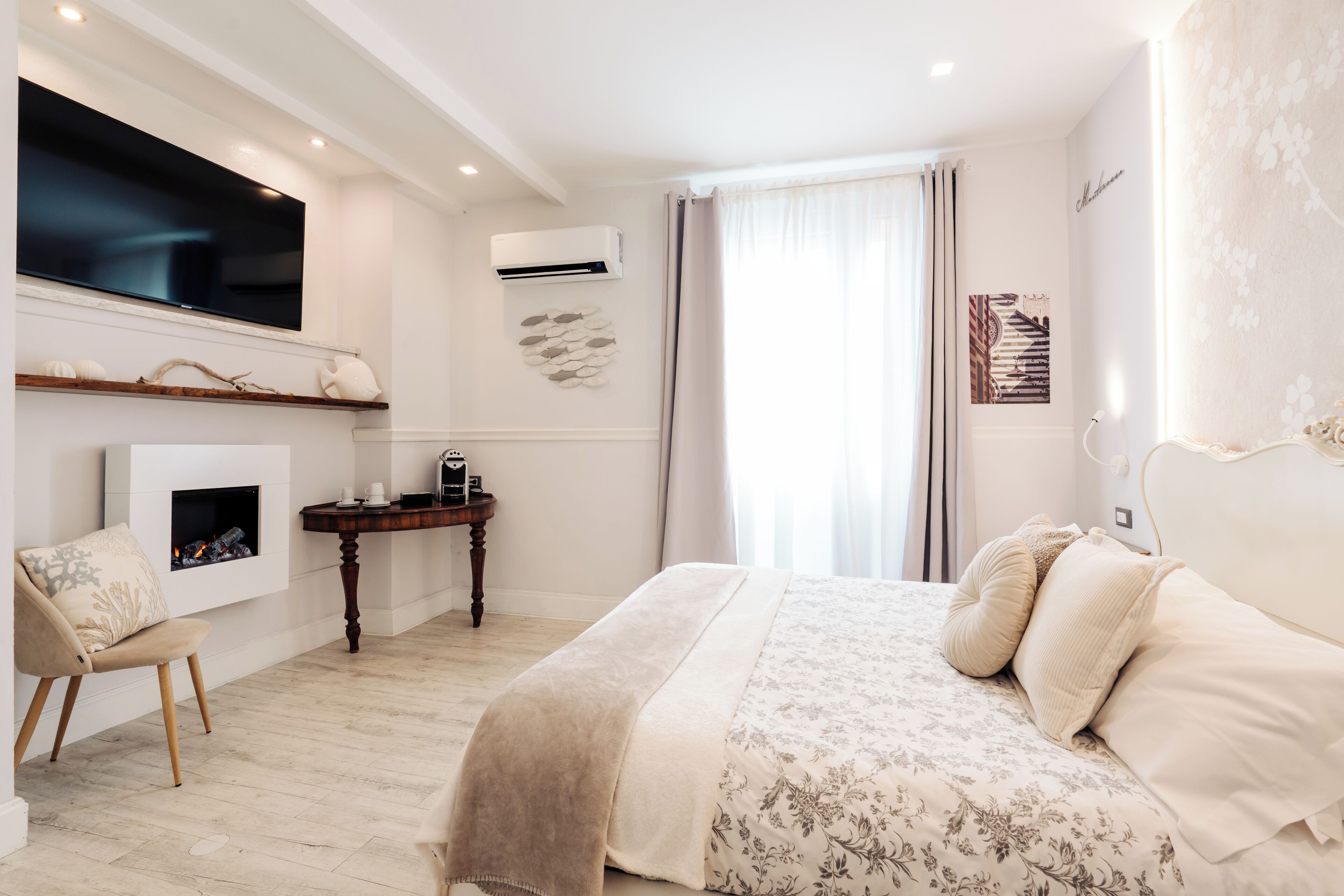 Un dormitorio con cama, televisor montado en la pared, chimenea y escritorio con silla.