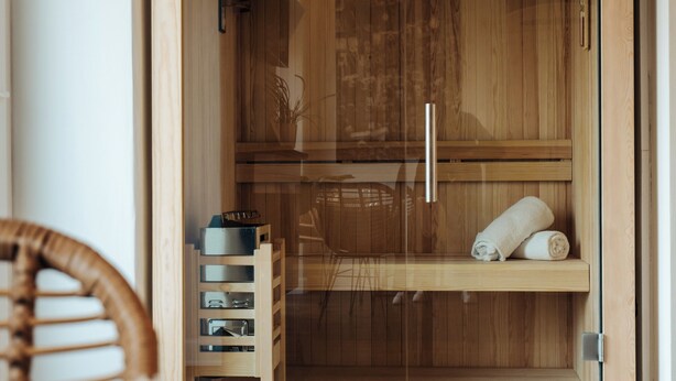 Un sauna de madera con puerta de vidrio, un estante con toallas y un banco de madera.