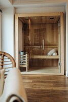 Un sauna de madera con puerta de vidrio, un estante con toallas y un banco de madera.