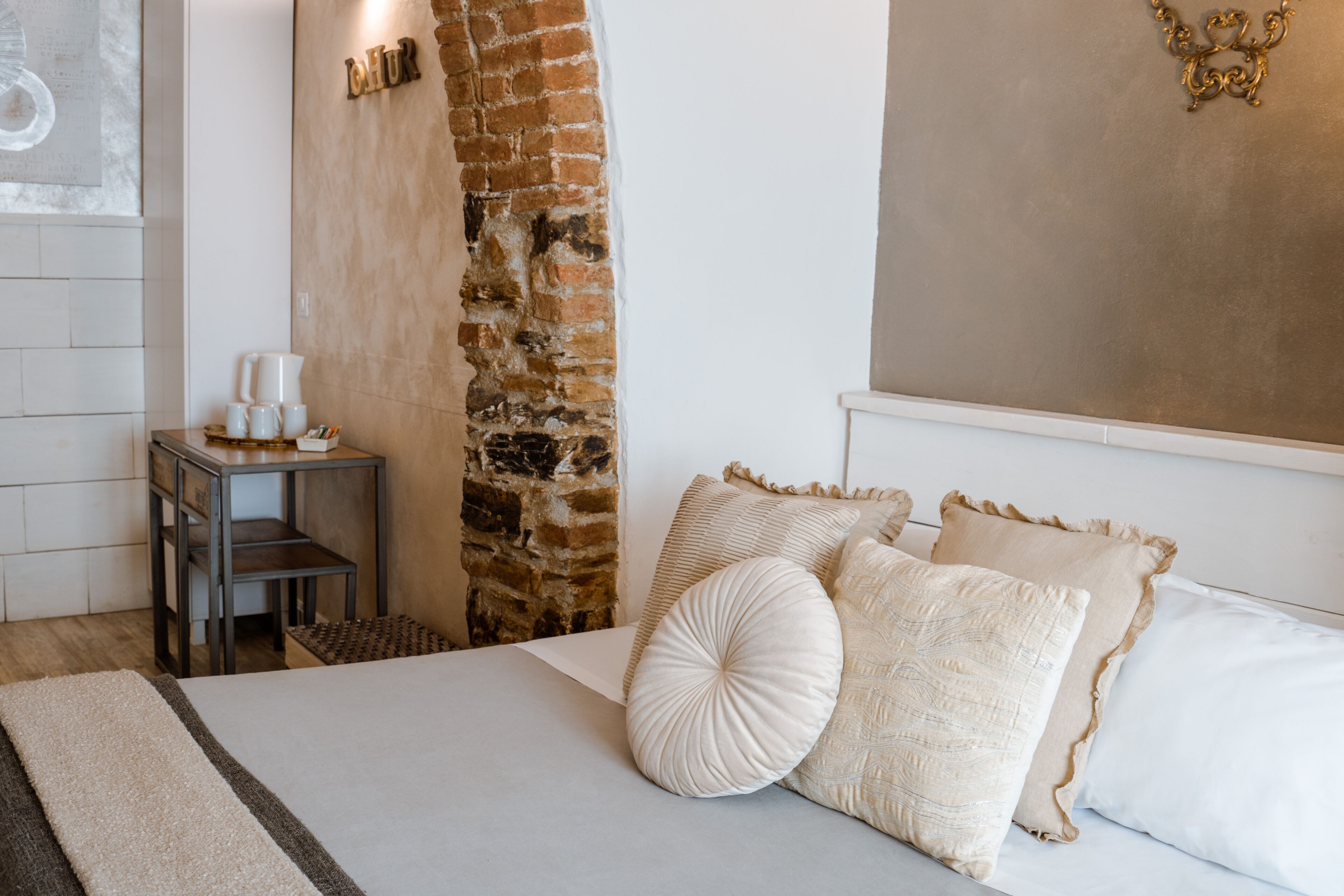 A bedroom with a brick wall, a wooden nightstand, a bed with white bedding, and a wall-mounted light fixture.