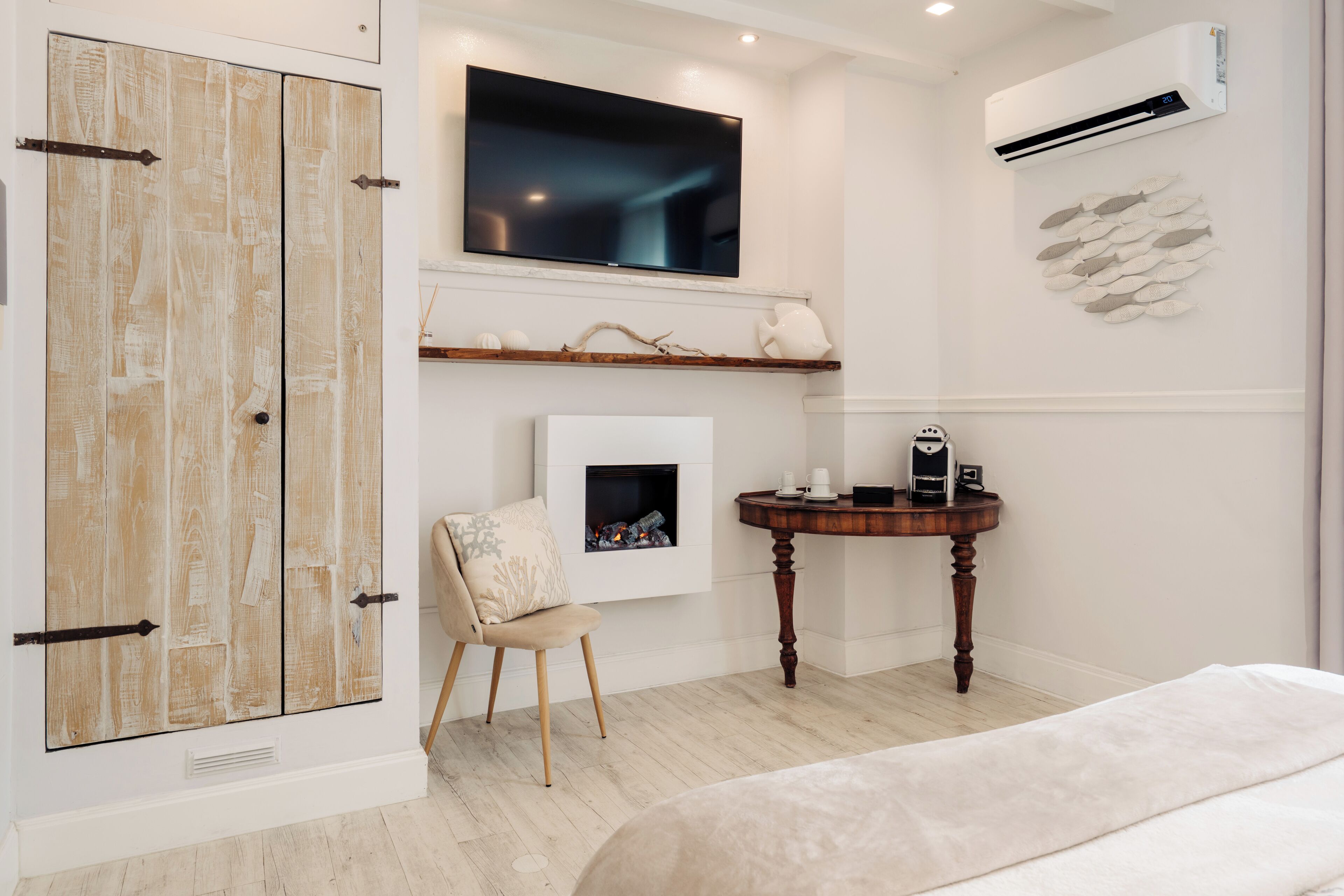 A bedroom with a bed, a TV mounted on the wall, a fireplace, and a small table with a cup and saucer.