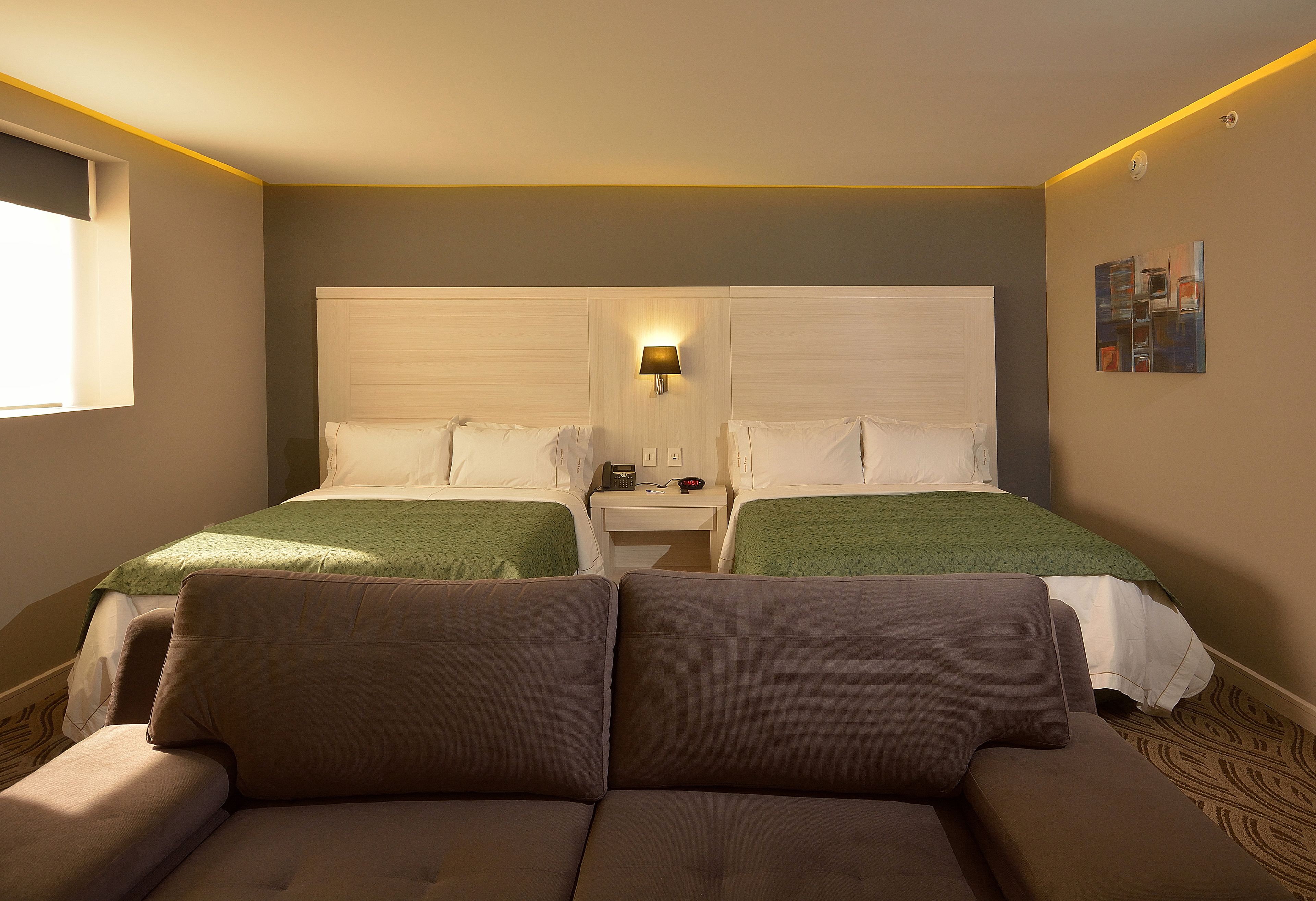 Een hotelkamer met twee bedden, een bank, een nachtkastje en een wandlamp.