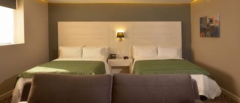 Een hotelkamer met twee bedden, een bank, een nachtkastje en een wandlamp.