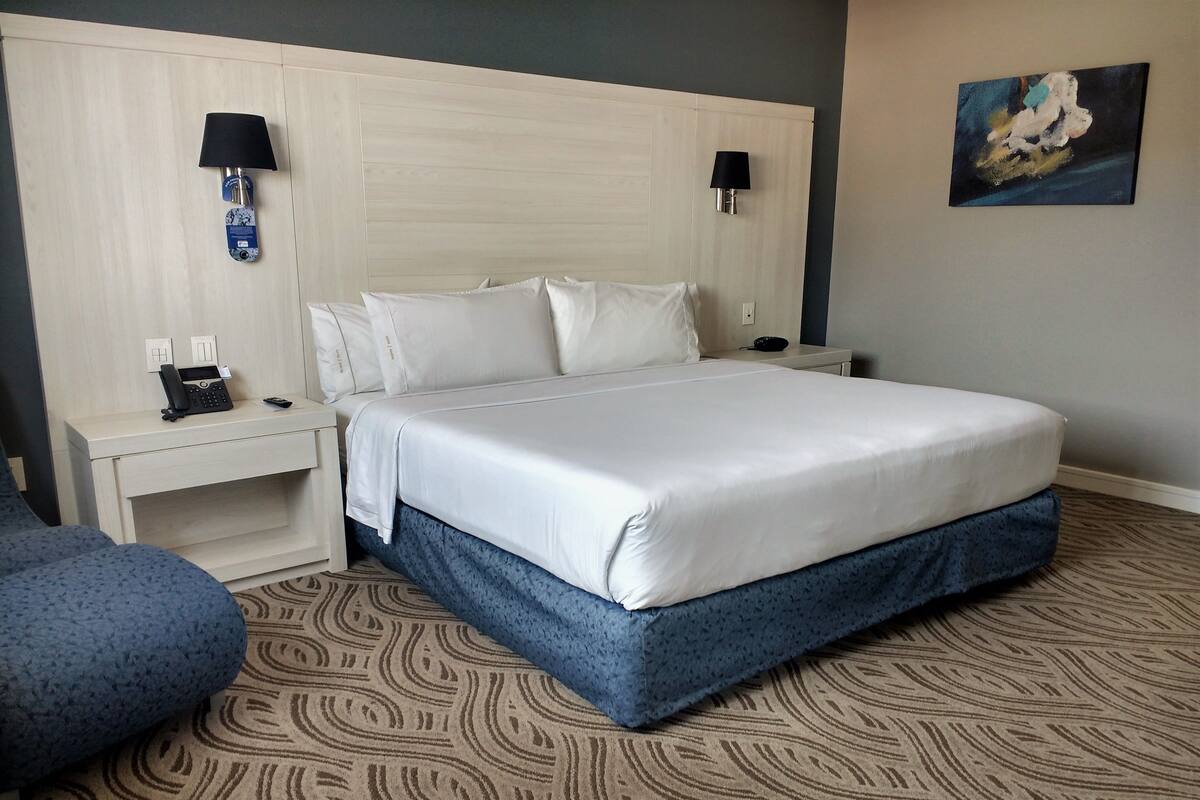 A hotel room with a large bed, two bedside tables, a phone, and a painting on the wall.