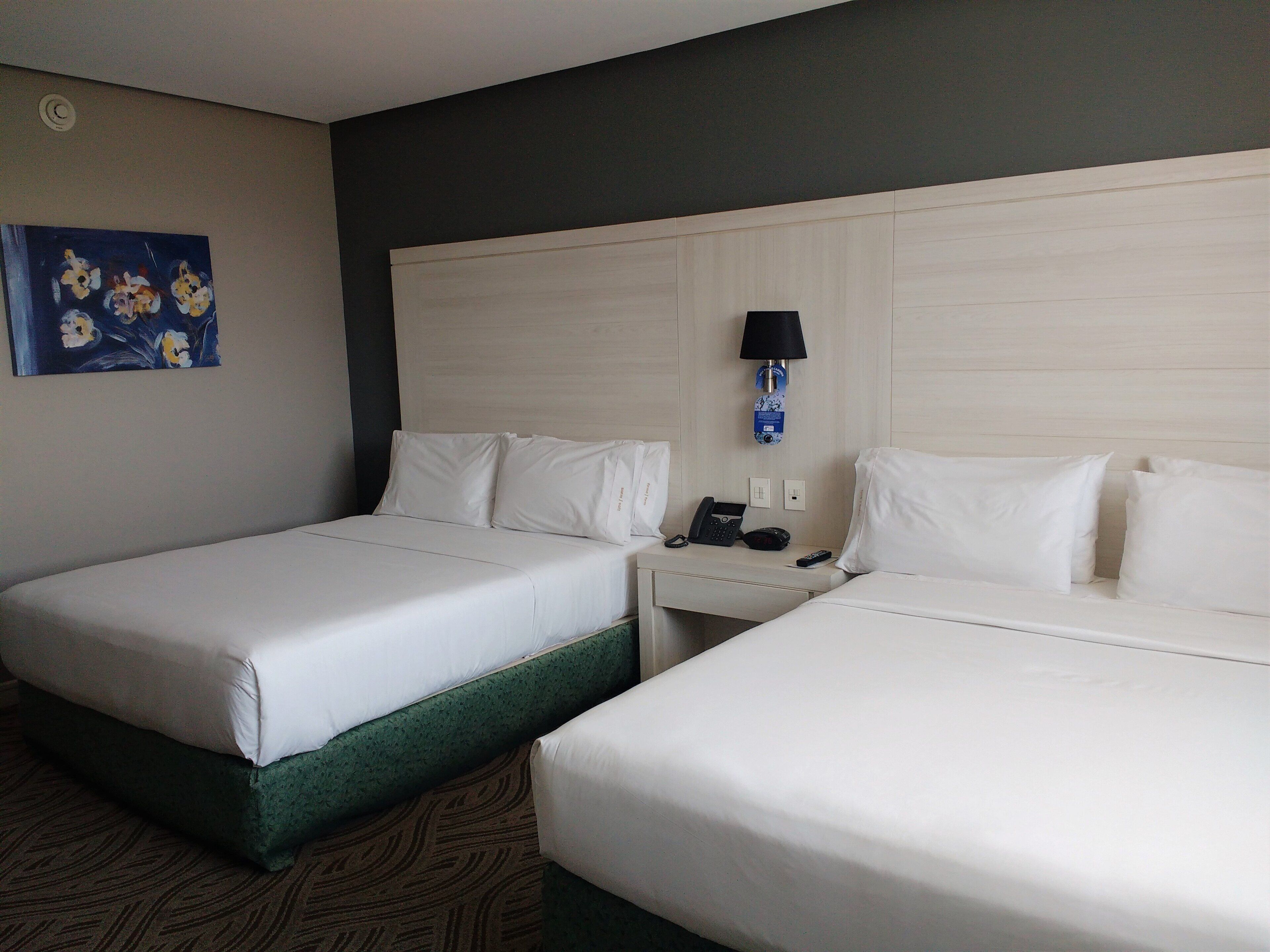 Habitación de hotel con dos camas, una mesita de noche con lámpara, teléfono y un cuadro en la pared.