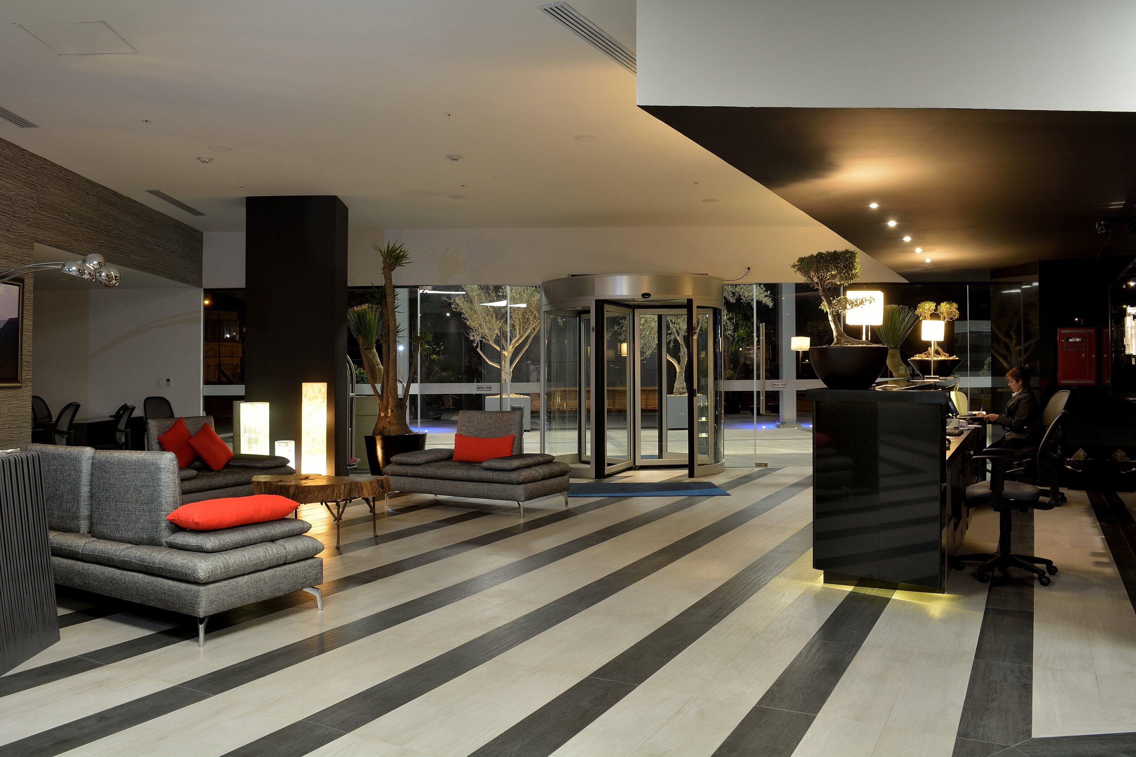 A modern lobby with a seating area, a reception desk, and a revolving door.