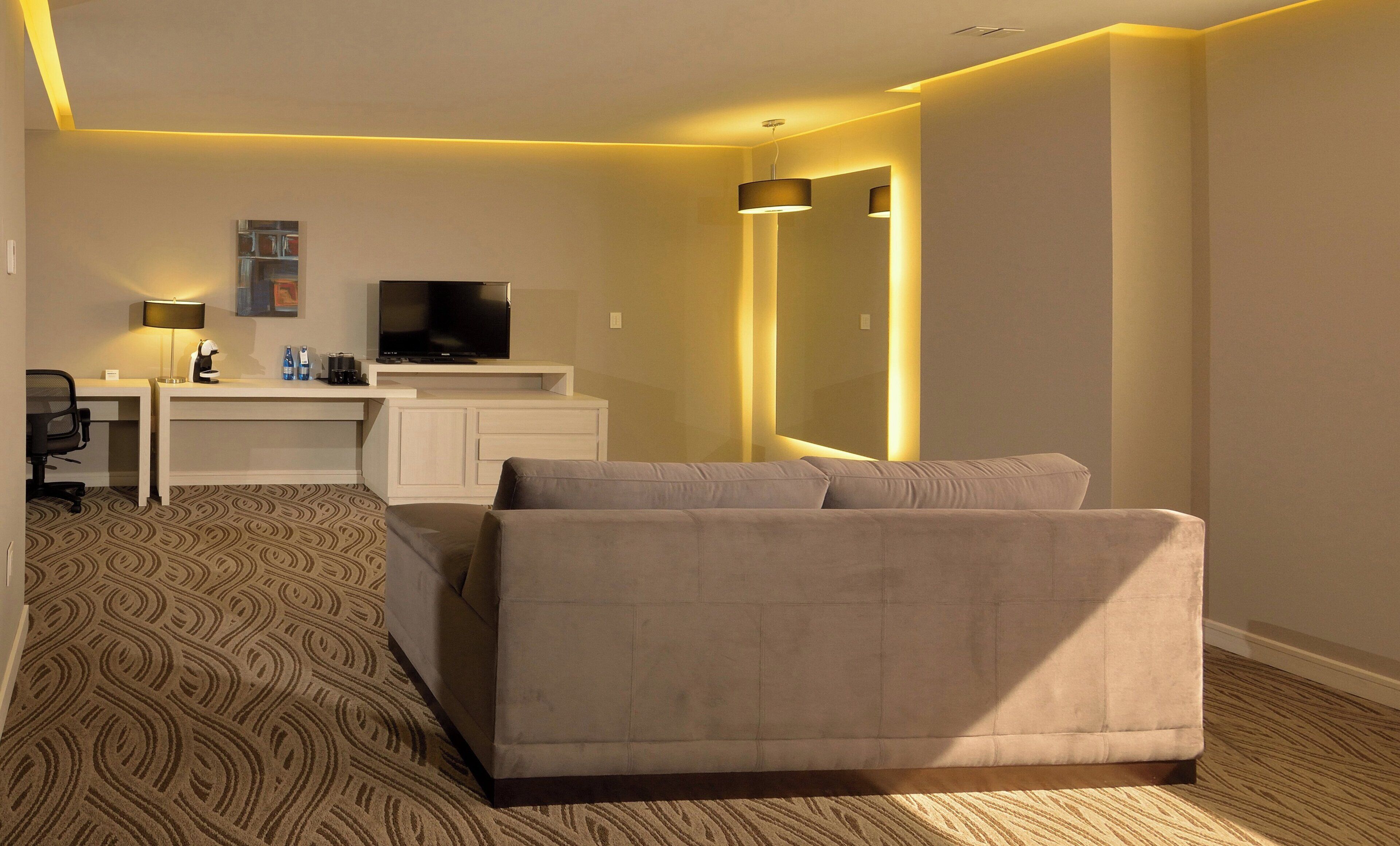 Una habitación de hotel con una cama, un escritorio con televisor, una lámpara y una alfombra estampada.