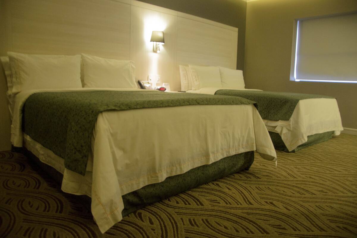 A hotel room with two beds, a headboard with a light, and a carpeted floor.