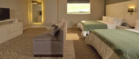 A hotel room with a sofa, two beds, a TV, and a window with a view.