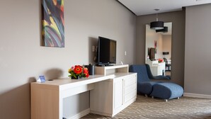 A modern hotel room with a flat-screen TV, a white console table, a blue sofa, and a patterned carpet.