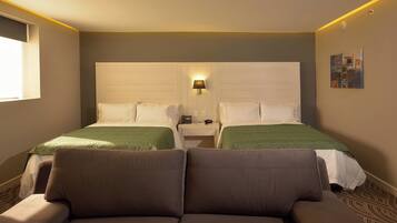 Una habitación de hotel con dos camas, un sofá, una mesita de noche con lámpara y un cuadro en la pared.
