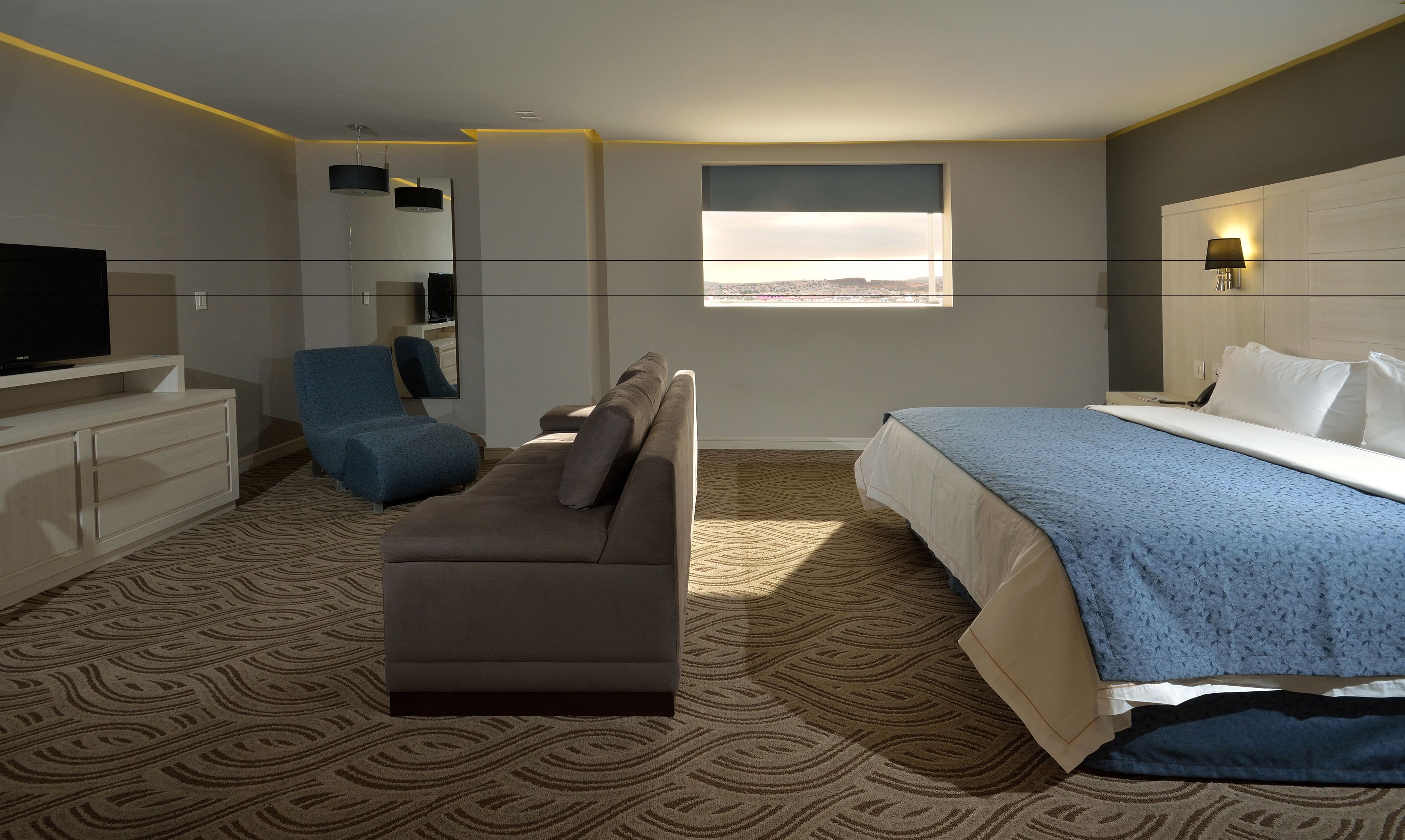 Une chambre d’hôtel avec un lit, un canapé, une télévision, un bureau et une fenêtre donnant sur un beau paysage.