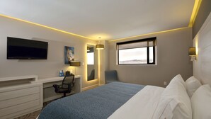 A hotel room with a bed, desk, chair, TV, and a window with a city view.