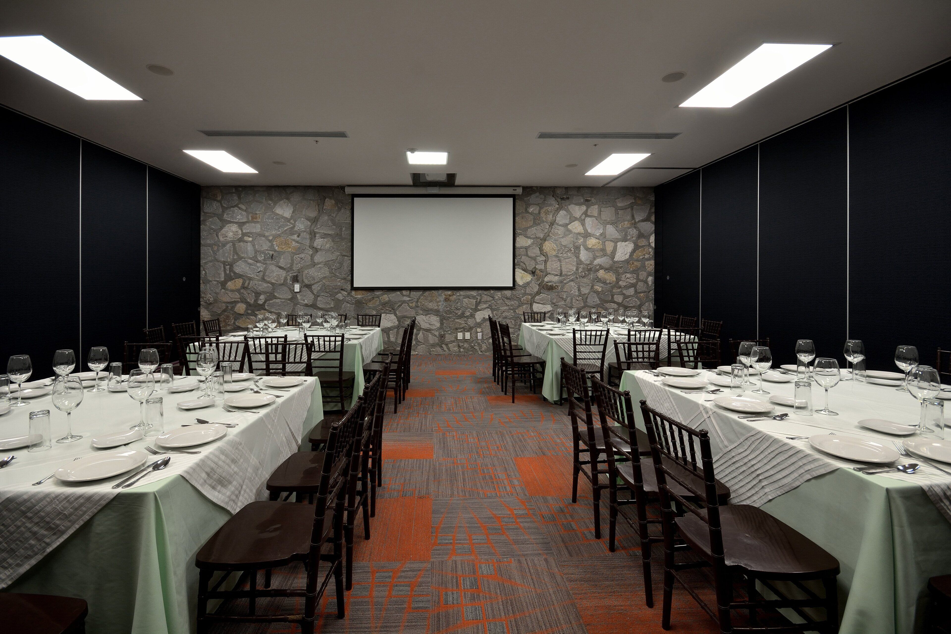 A conference room with tables set for dining, a projector screen, and a stone wall.