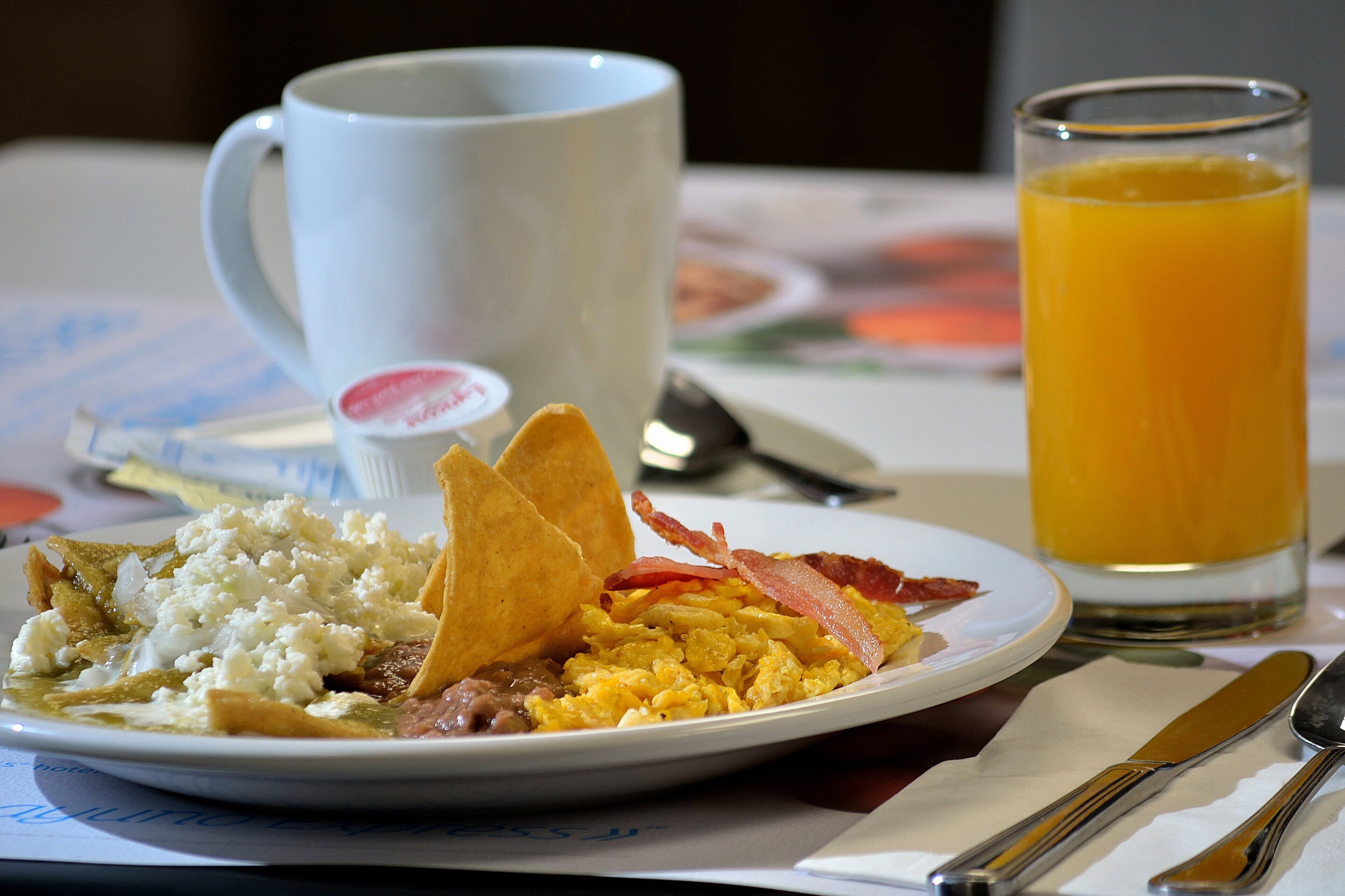 Prato de café da manhã com ovos mexidos, bacon, torradas e um copo de suco de laranja.
