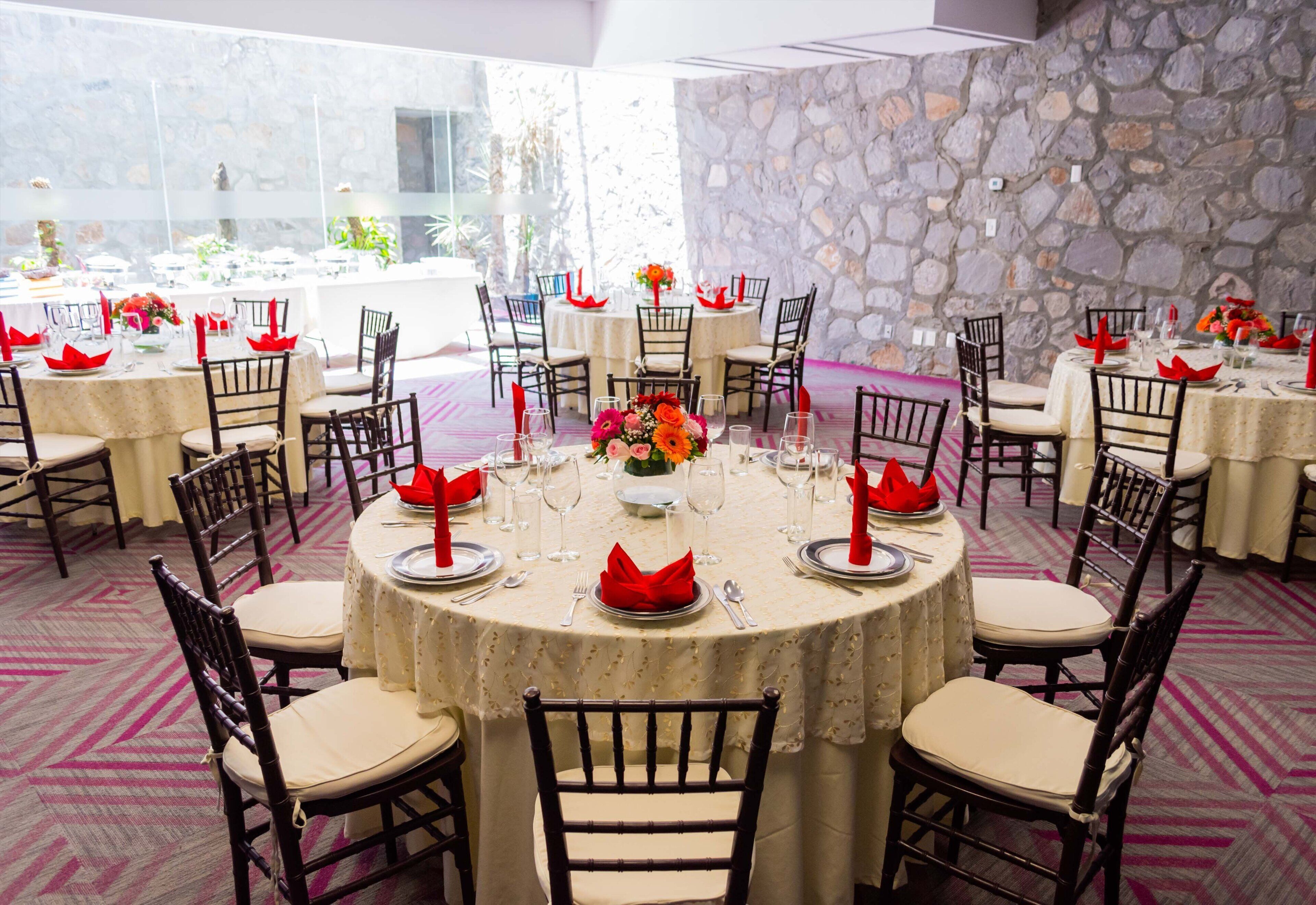 A banquet hall with round tables, chairs, and floral centerpieces.