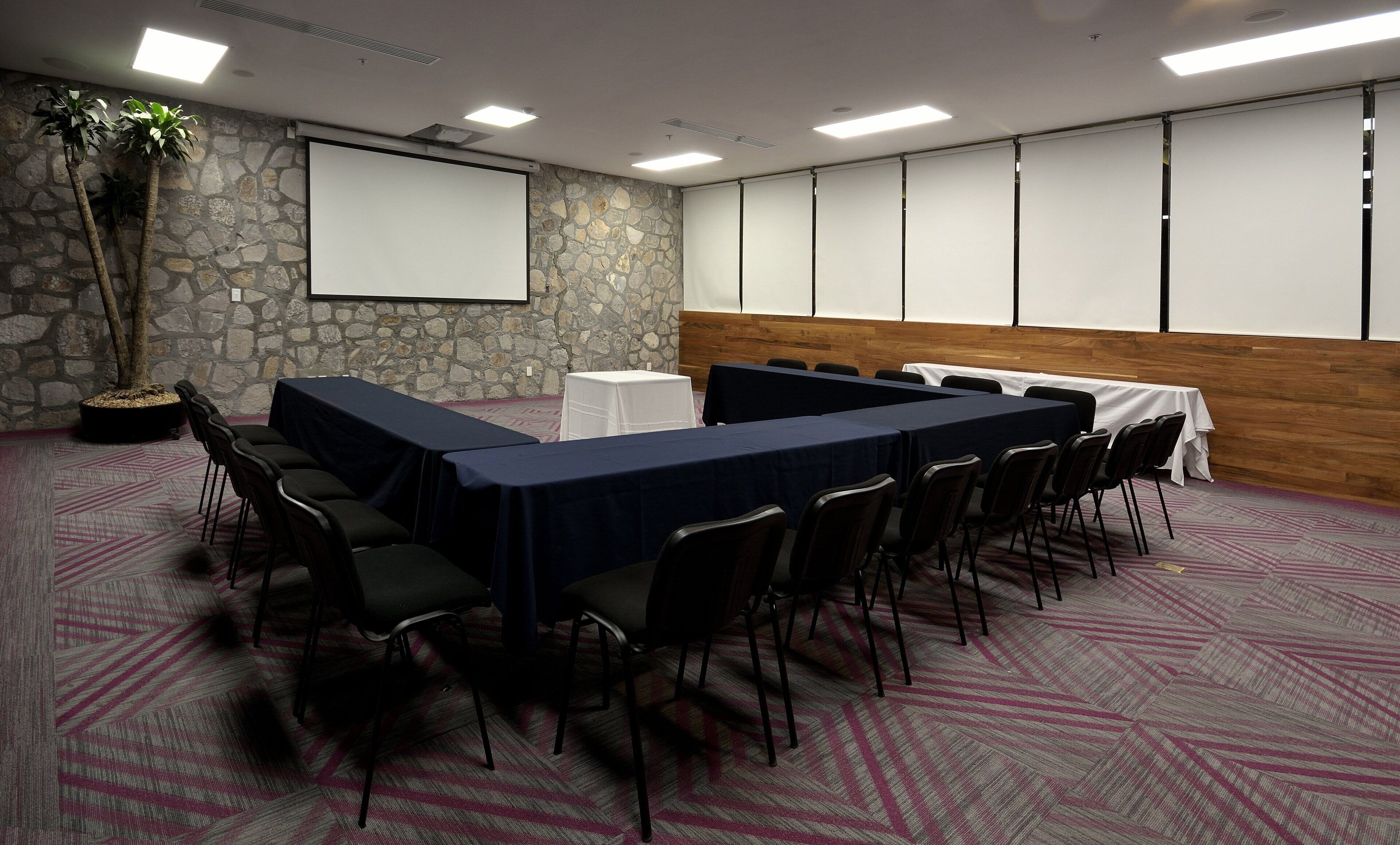 A conference room with a long table, chairs, a projector screen, and a stone wall.