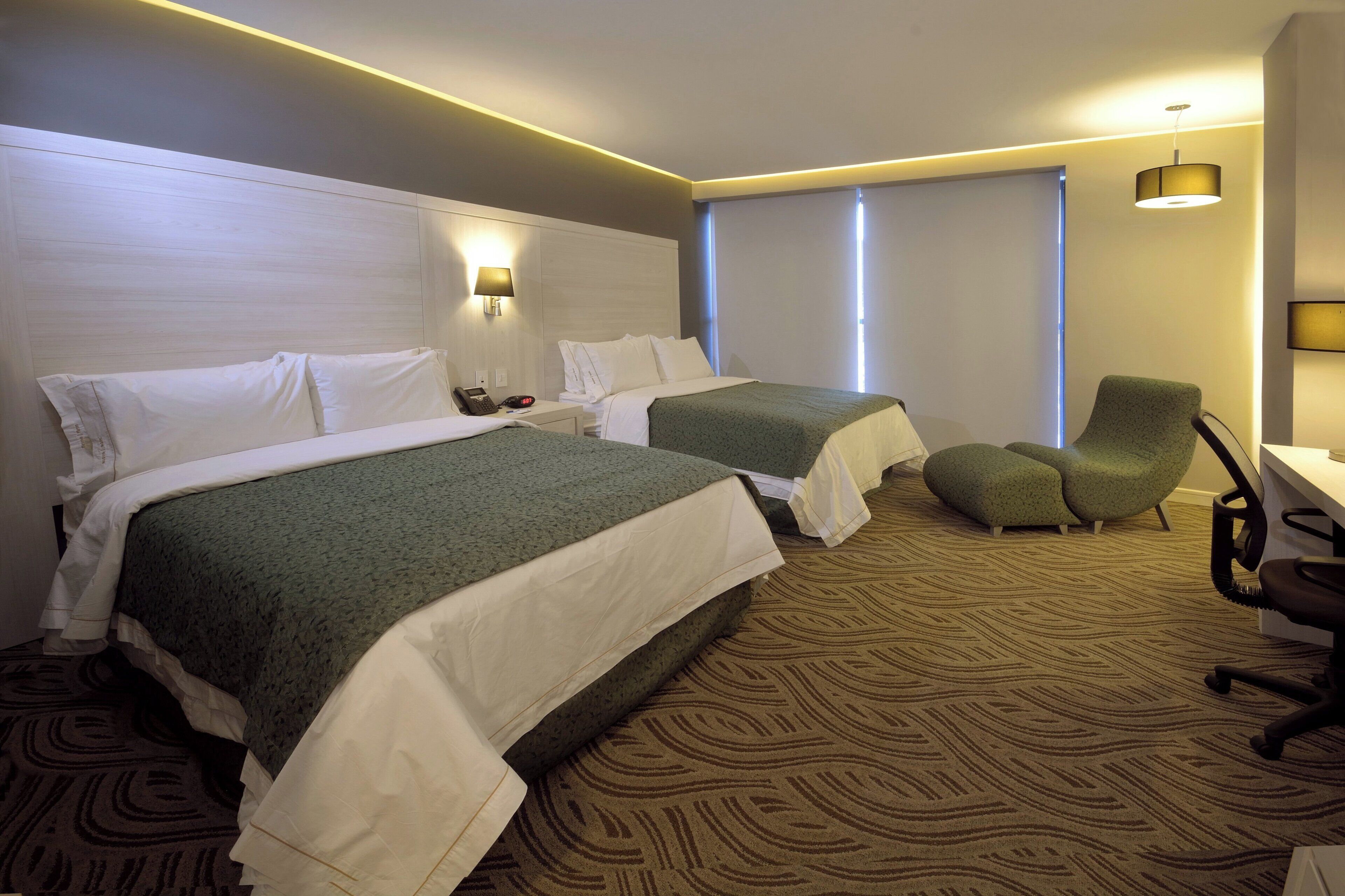 A hotel room with two beds, a desk, a chair, and a window.