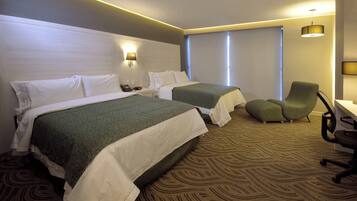 A hotel room with two beds, a desk, a chair, and a window.