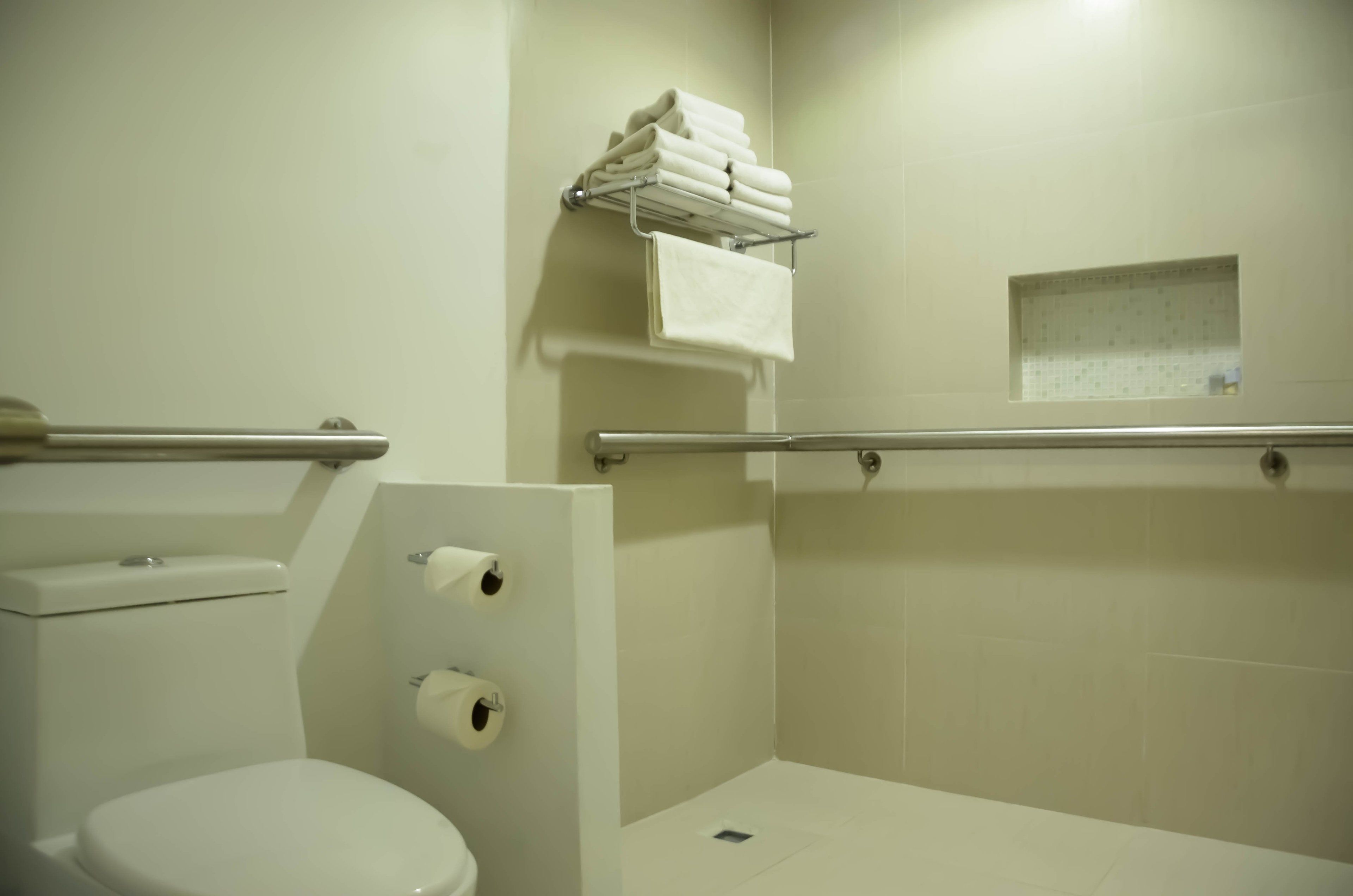 Un baño con inodoro, secamanos y un perchero con toallas dobladas.