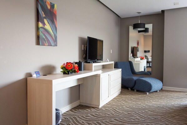 A modern hotel room with a flat-screen TV, a white console table with a vase of flowers, a blue sofa, and a patterned carpet.
