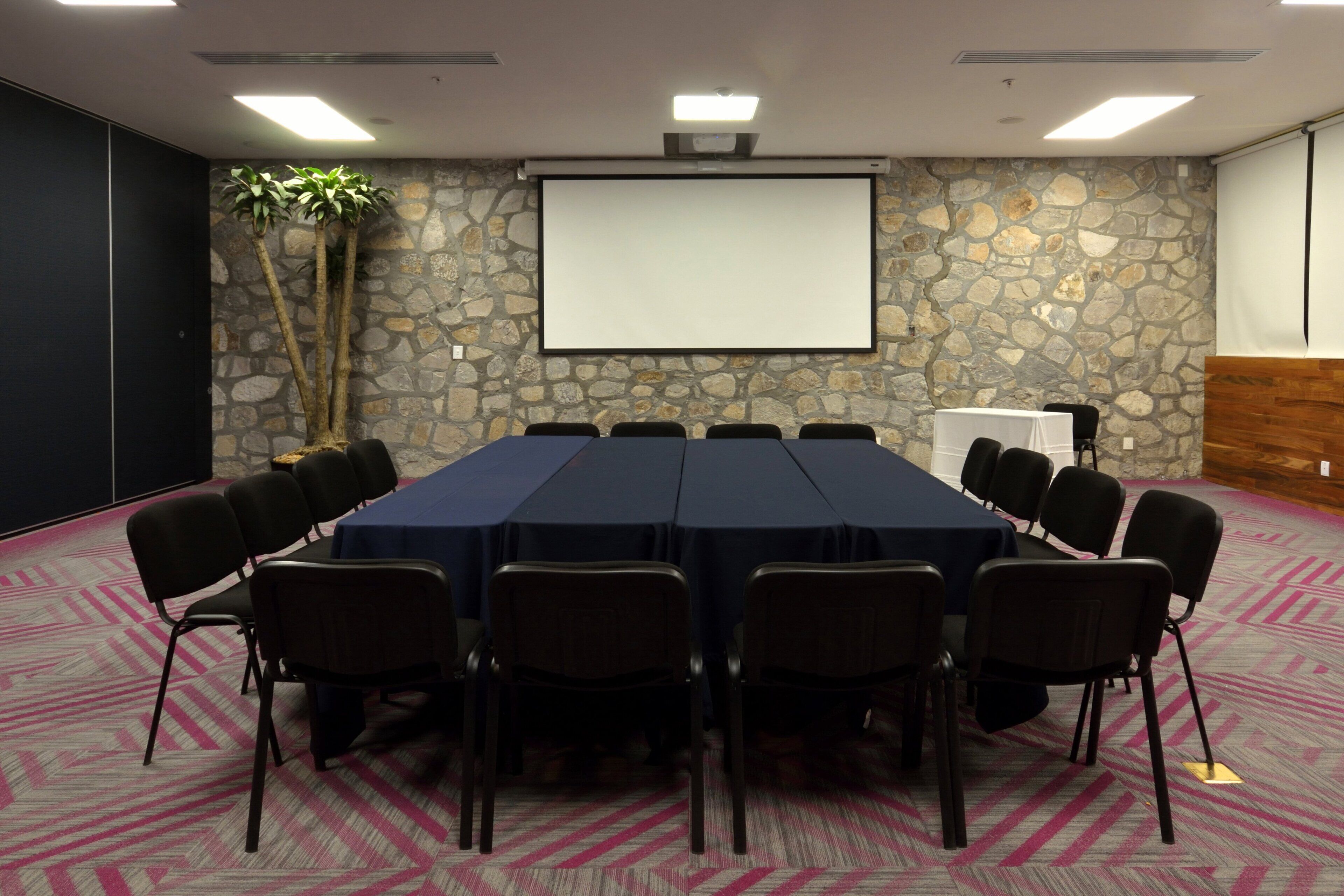Ein Konferenzraum mit einem langen Tisch, Stühlen, einer Projektionsleinwand und einer Steinsäule.