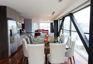 A modern dining area with a glass table surrounded by upholstered chairs, a red sofa in the background, and a city view through large windows. - Holiday Inn Express Pachuca by IHG (Pachuca)
