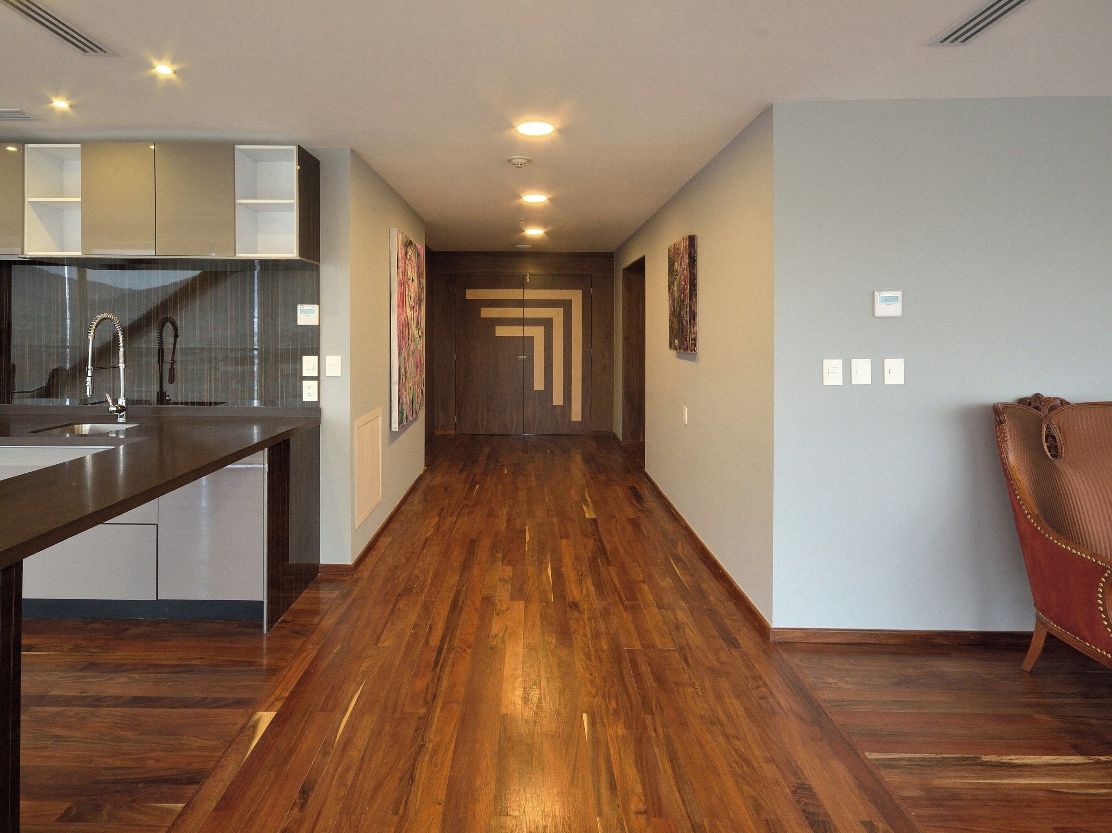 Un interior moderno con zona de cocina, suelo de madera y un pasillo que conduce a una puerta.