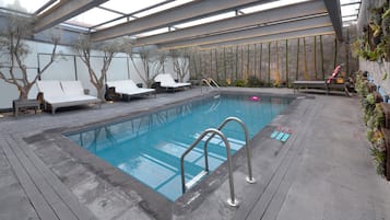 An indoor swimming pool with lounge chairs and a stone wall.