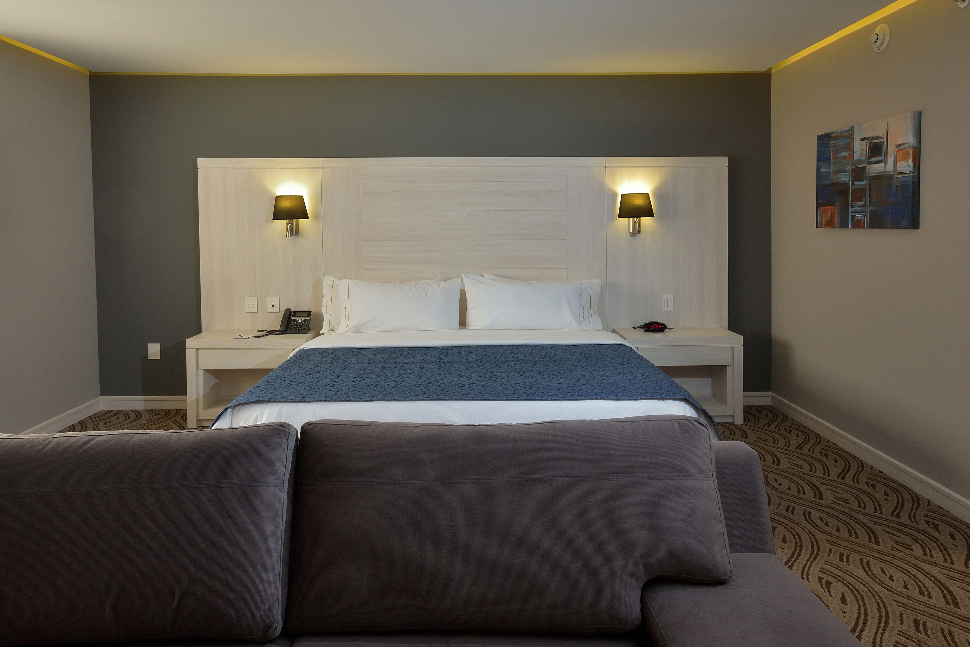 Ein Hotelzimmer mit einem großen Bett, zwei Nachttischlampen, einem Nachttisch und einem Kopfteil.