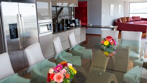 A modern kitchen with stainless steel appliances, a glass dining table with chairs, and a red sofa in the living area.