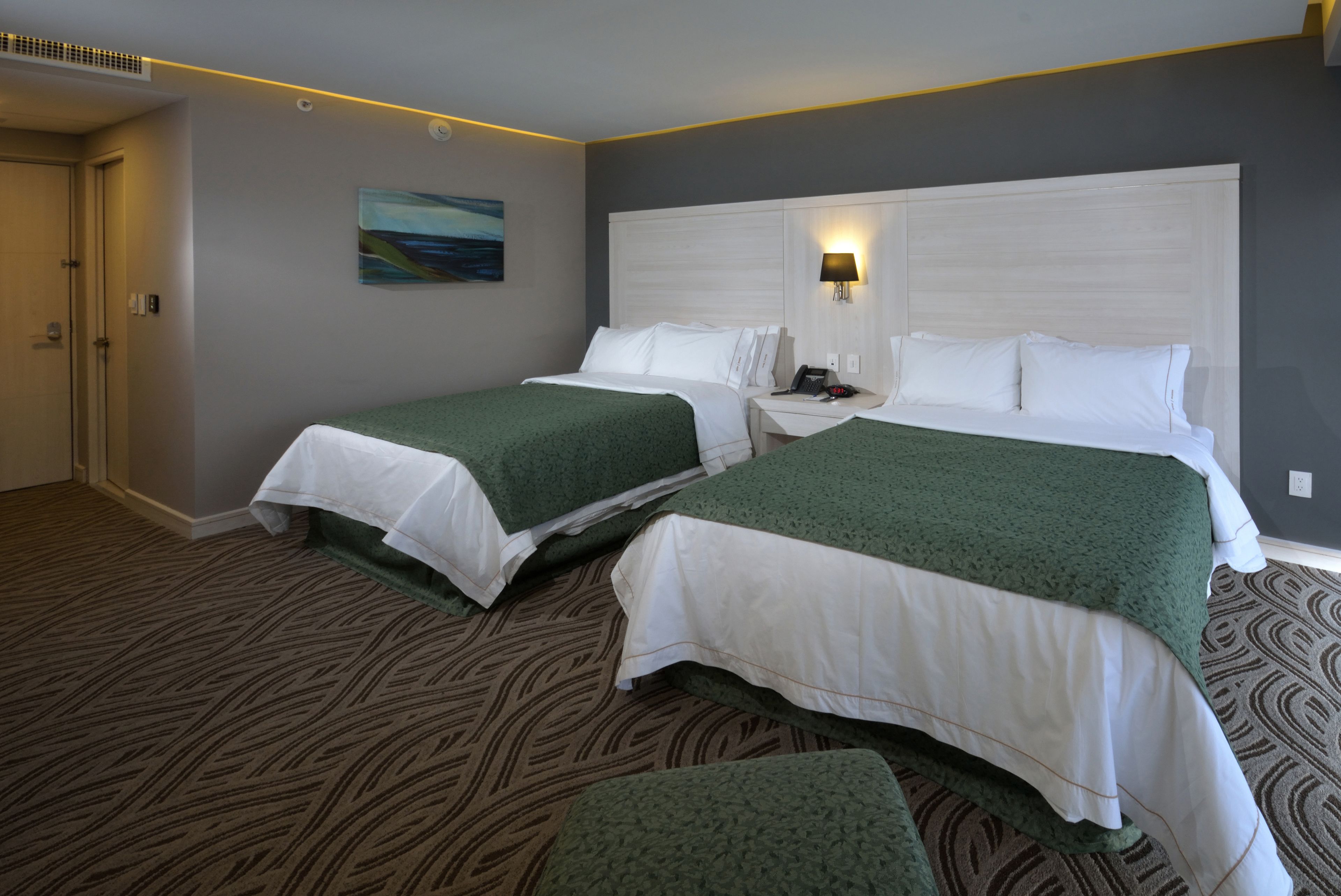 A hotel room with two beds, a painting on the wall, and a patterned carpet.