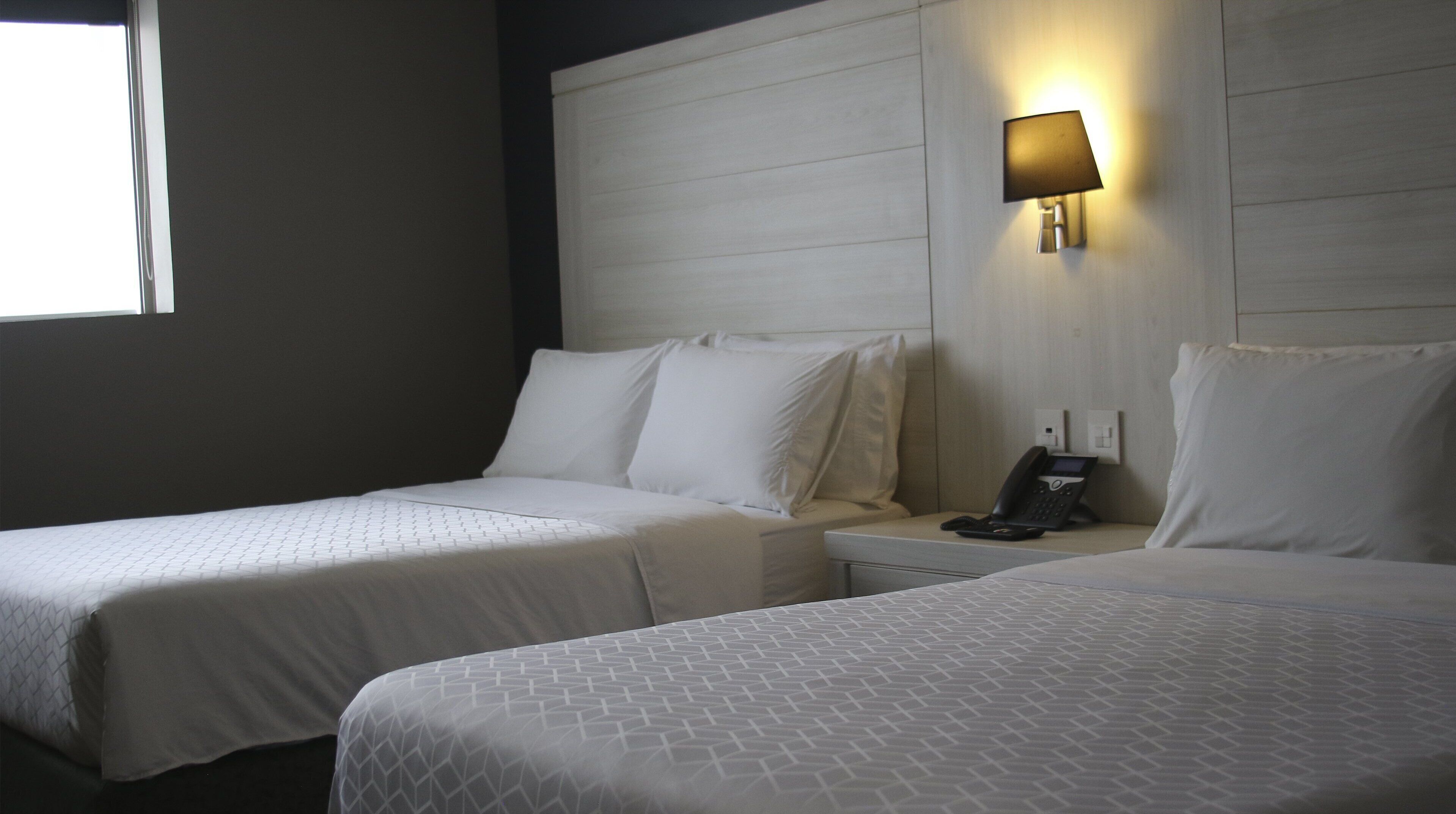 Habitación de hotel con dos camas, una mesita de noche con teléfono y una lámpara de pared.