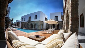 A poolside area with lounge chairs and a wooden deck, overlooking a pool and a building with stone arches. - Saraya Bodrum Hotel (Bodrum)