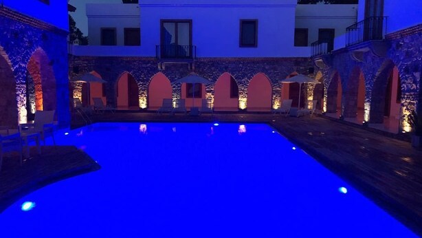 A swimming pool with a stone wall and arches, surrounded by lounge chairs and umbrellas. - Saraya Bodrum Hotel (Bodrum)