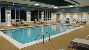 Una piscina interior con agua cristalina, rodeada de sillones de descanso y una estación de salvavidas.