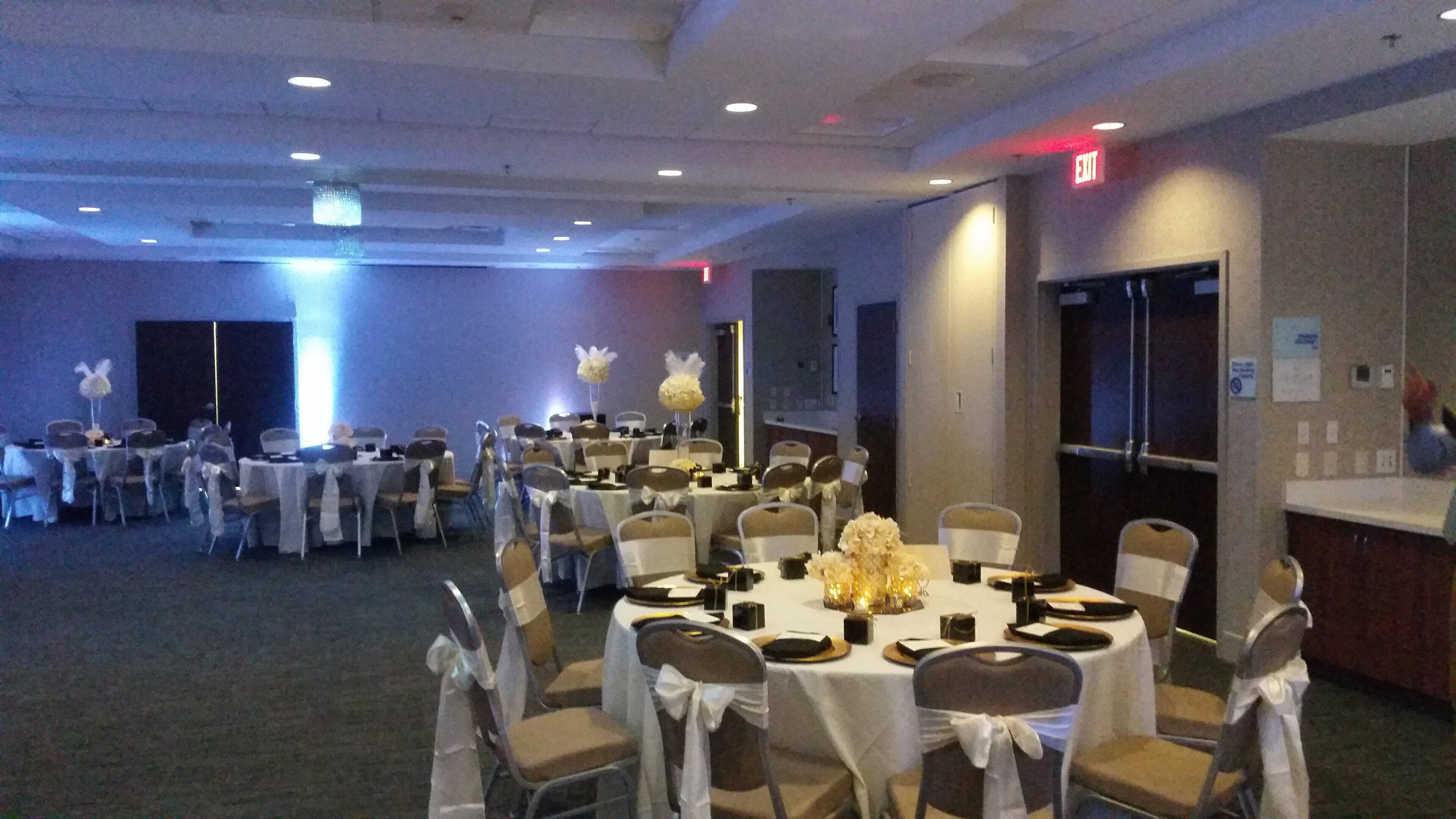 A banquet hall with round tables, chairs, and white tablecloths.