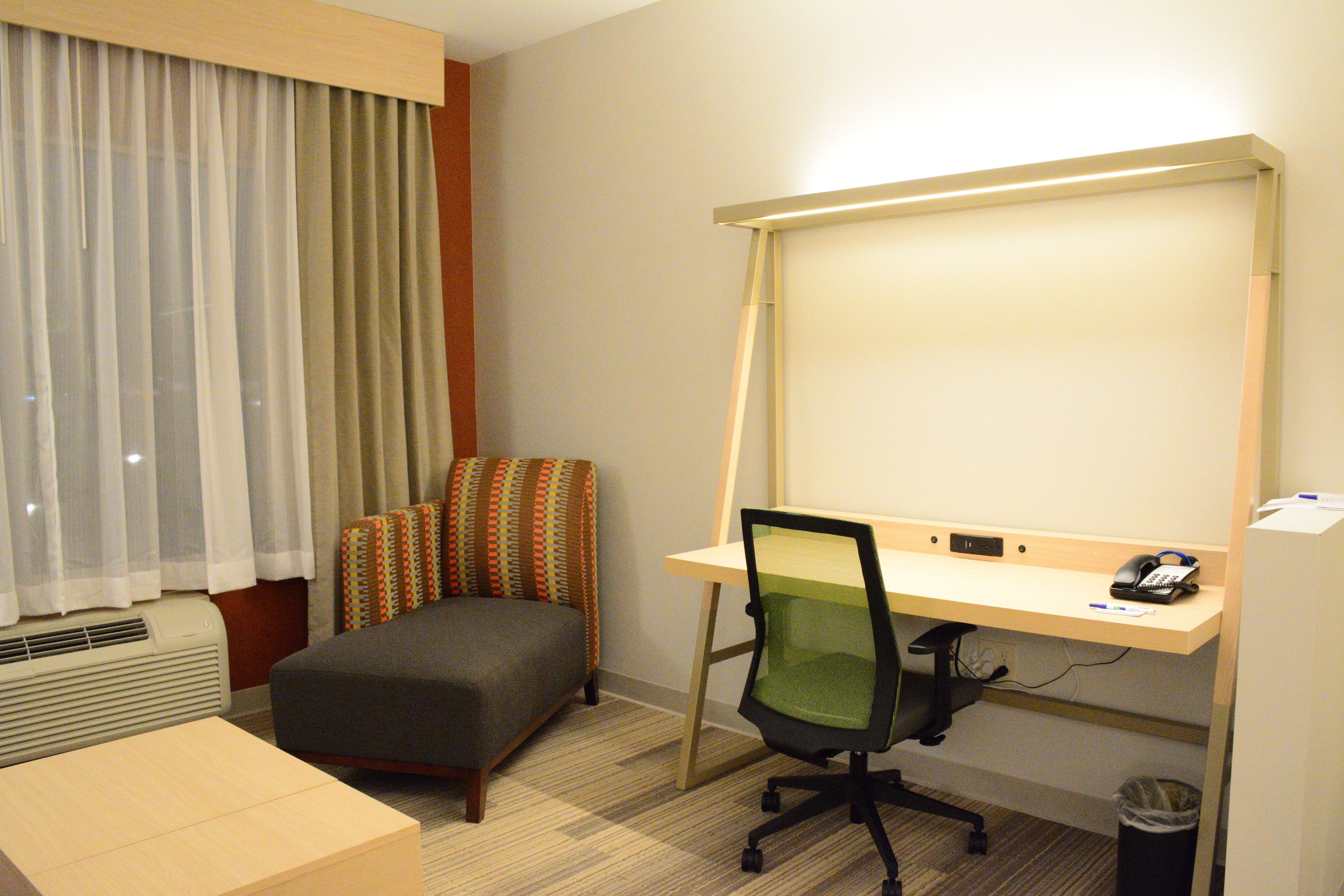 A hotel room with a desk, chair, and a large window with curtains.