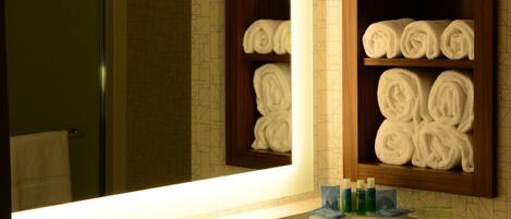 A bathroom with a large mirror, a sink, and shelves with rolled towels.