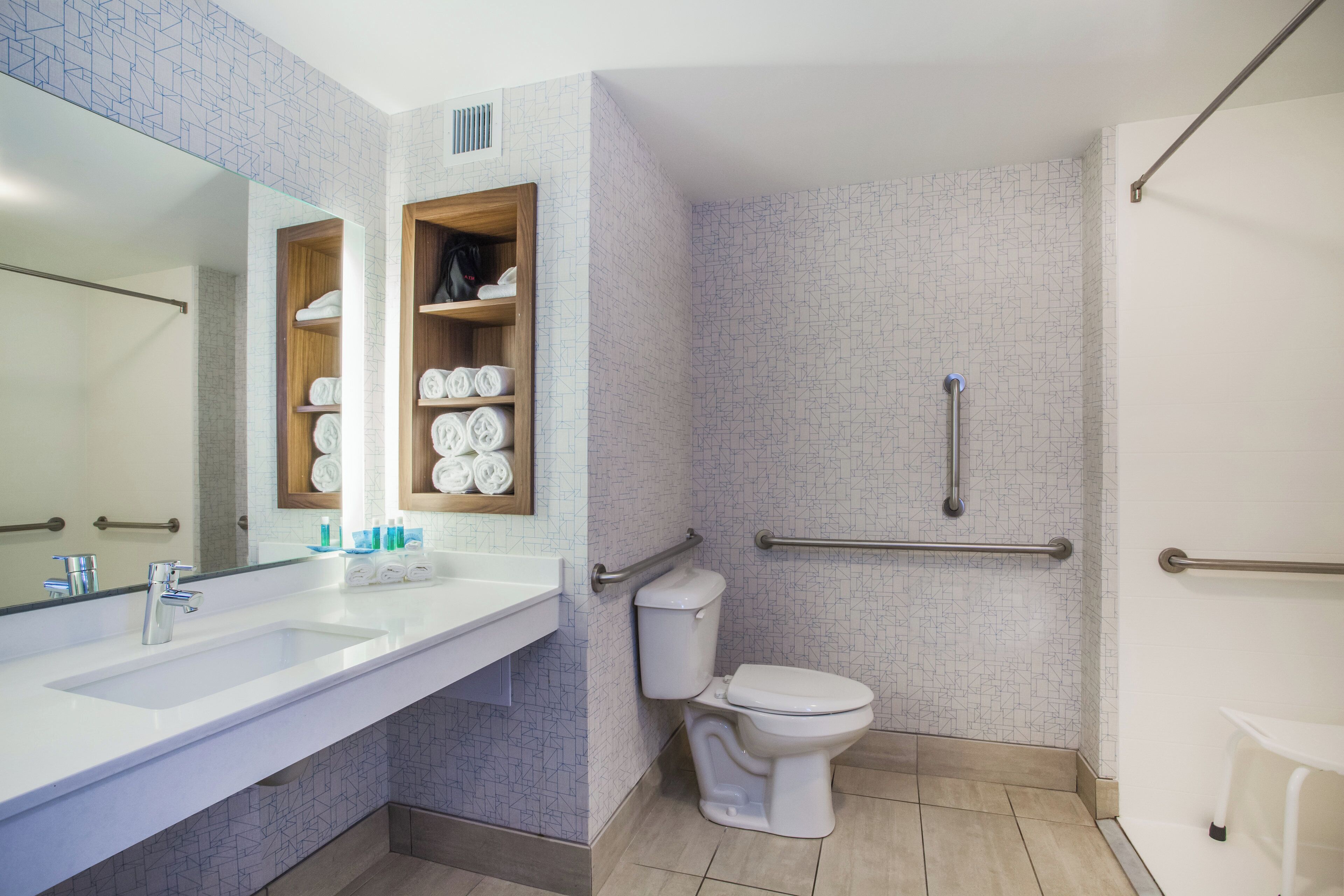 A modern bathroom with a large mirror, a white sink, a toilet, and a shower area.